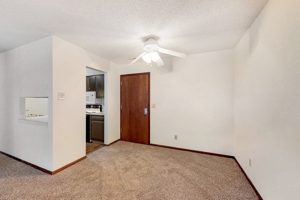 an empty living room with a ceiling fan and a kitchen