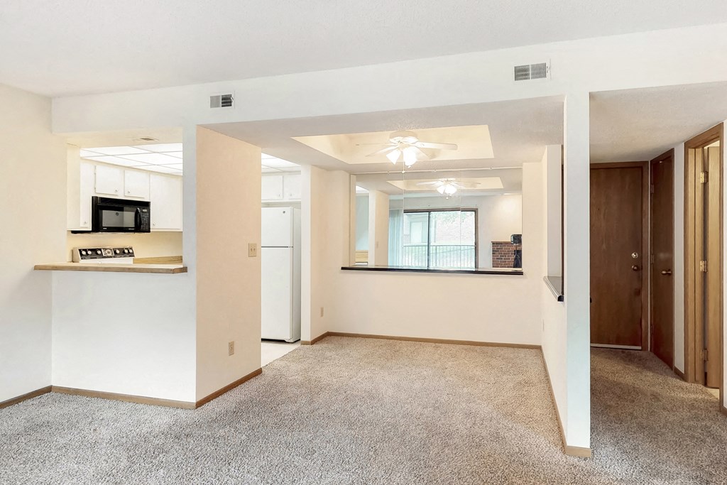 an empty living room with a kitchen and a ceiling fan