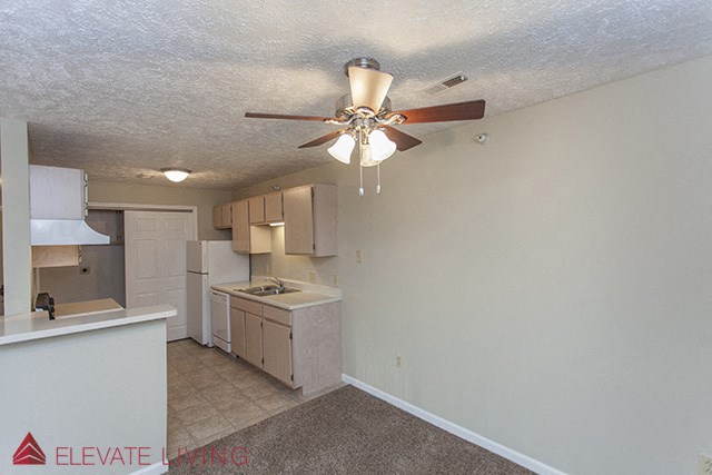 an empty kitchen with a ceiling fan and a kitchen with white cabinets