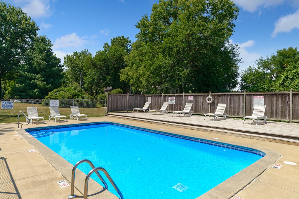 a swimming pool with chairs around it and trees in the background