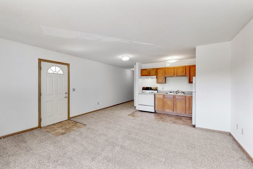 an empty living room with a kitchen with a white door