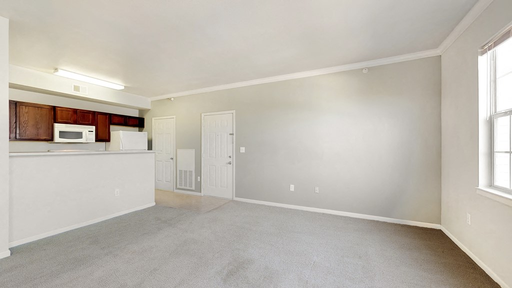 the living room and kitchen of an apartment with white walls and carpet