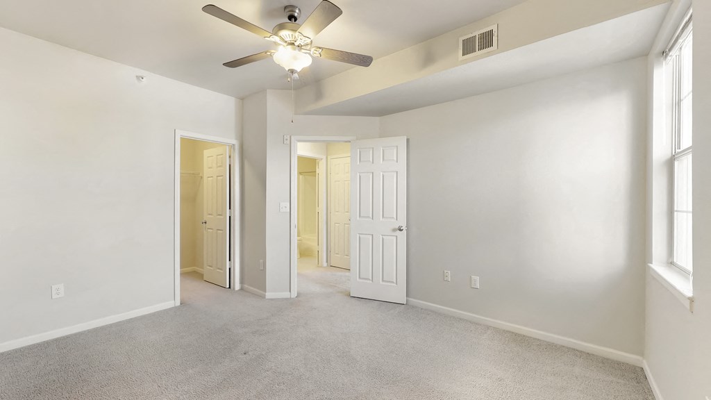 an empty living room with a ceiling fan and a door to a hallway