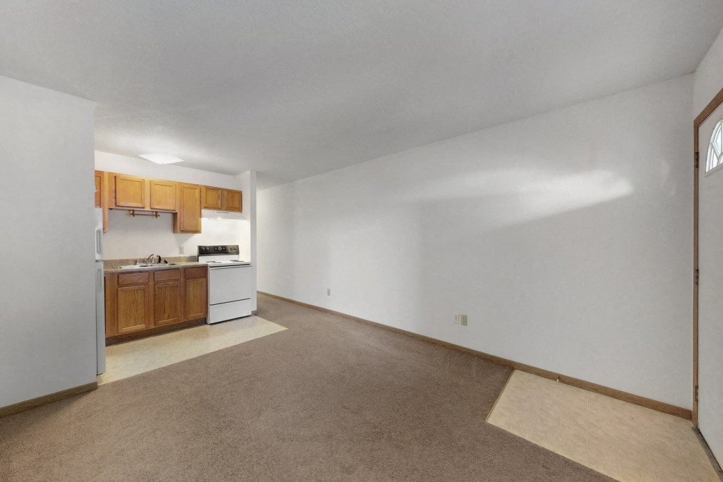 the living room and kitchen of an apartment with white walls and wood cabinets
