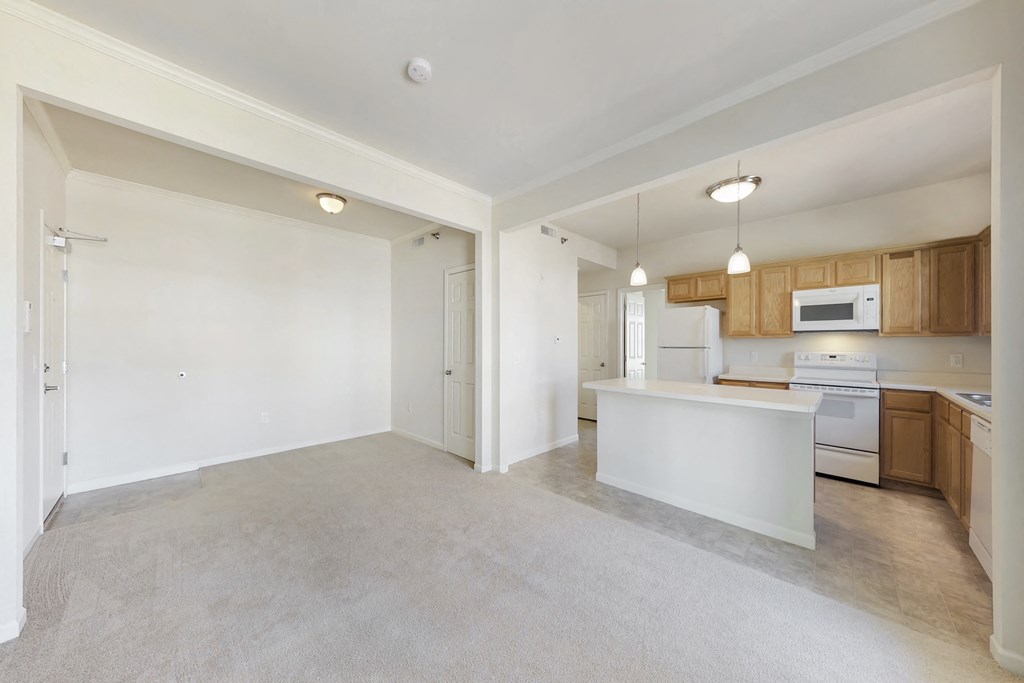 an empty living room and kitchen with white appliances and wood cabinets