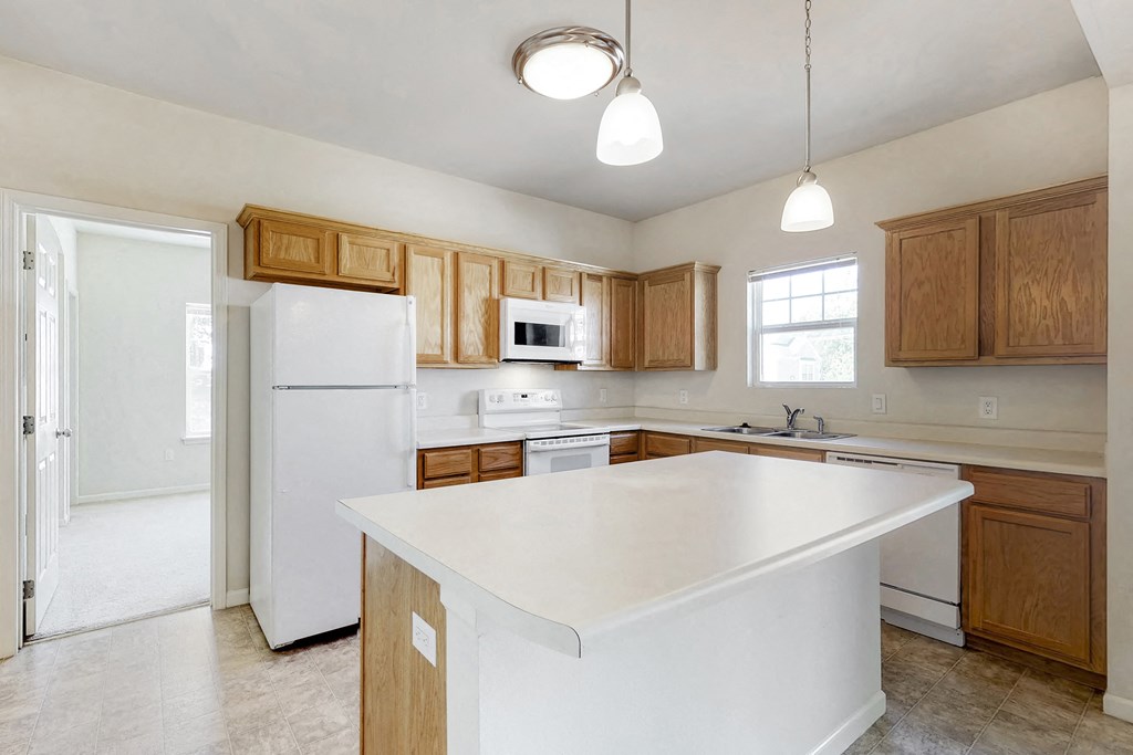 an empty kitchen with a large white island and wooden cabinets