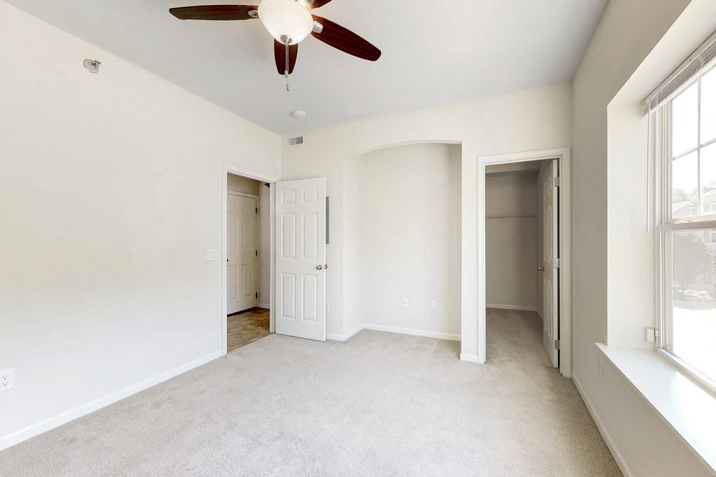 an empty living room with a ceiling fan and a door to a hallway