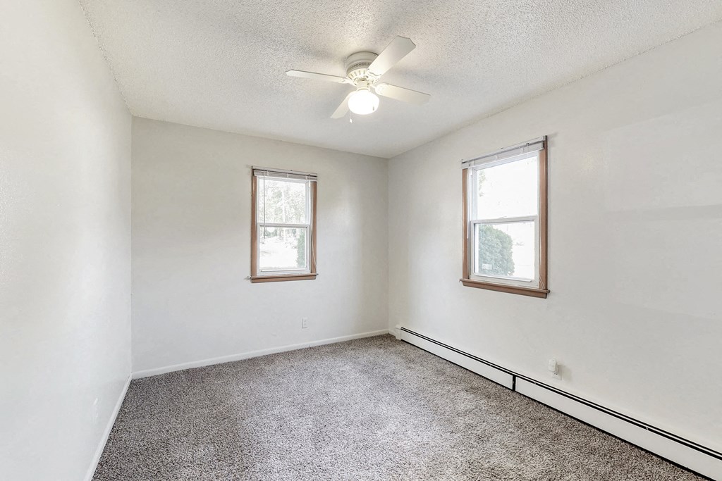 an empty room with two windows and a ceiling fan