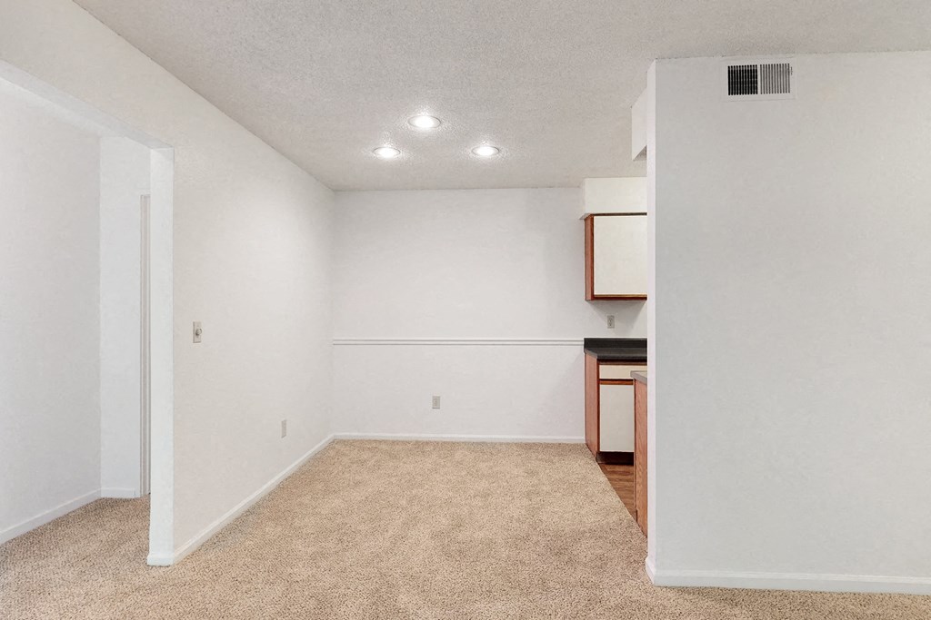 an empty living room with white walls and a kitchen