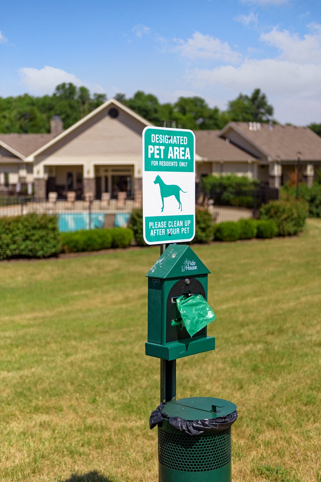 a green parking meter in the middle of a field with a house in the background
