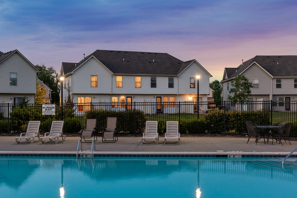 a swimming pool with chairs and a house in the background