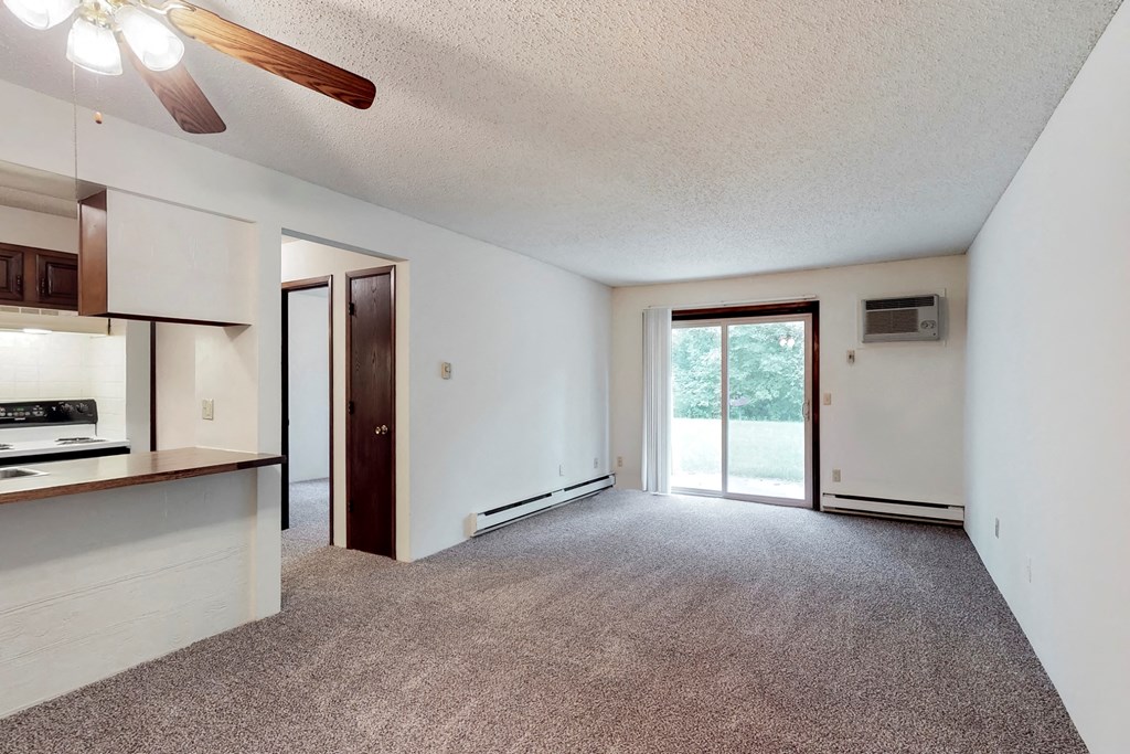 an empty living room with a kitchen and a sliding glass door