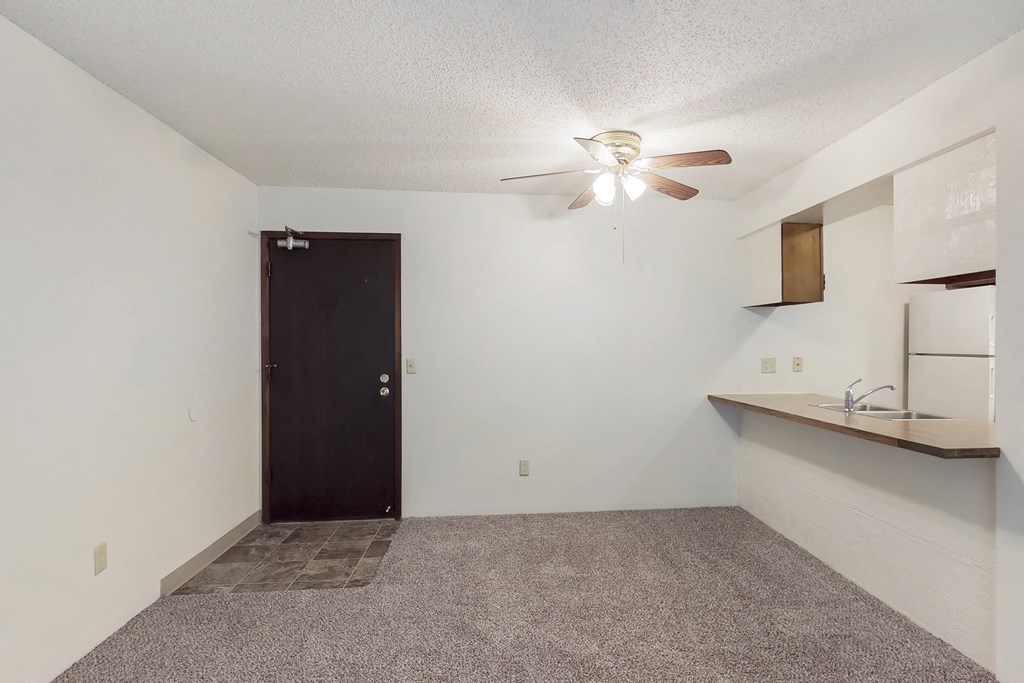 an empty living room with a ceiling fan and a kitchen