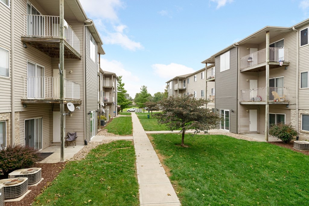 the view of an apartment building with a sidewalk and green grass