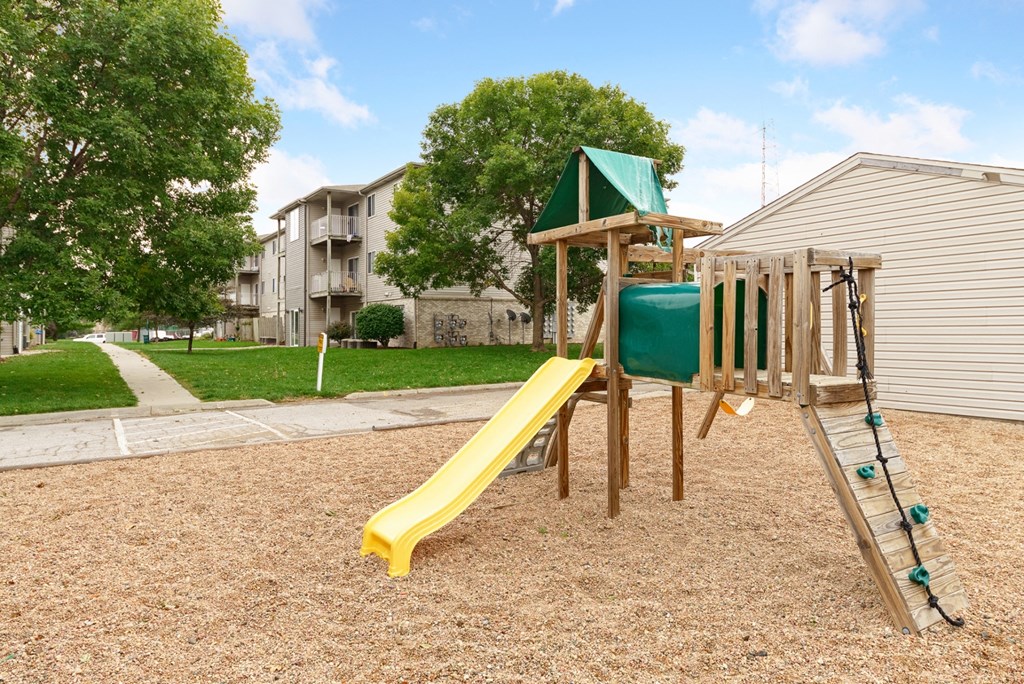 a playground with a slide and swings in front of an apartment building