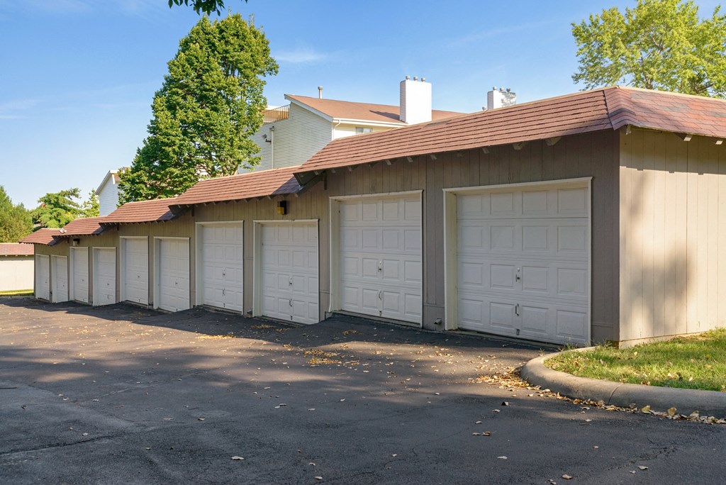 a row of garages with white doors and a house in the background