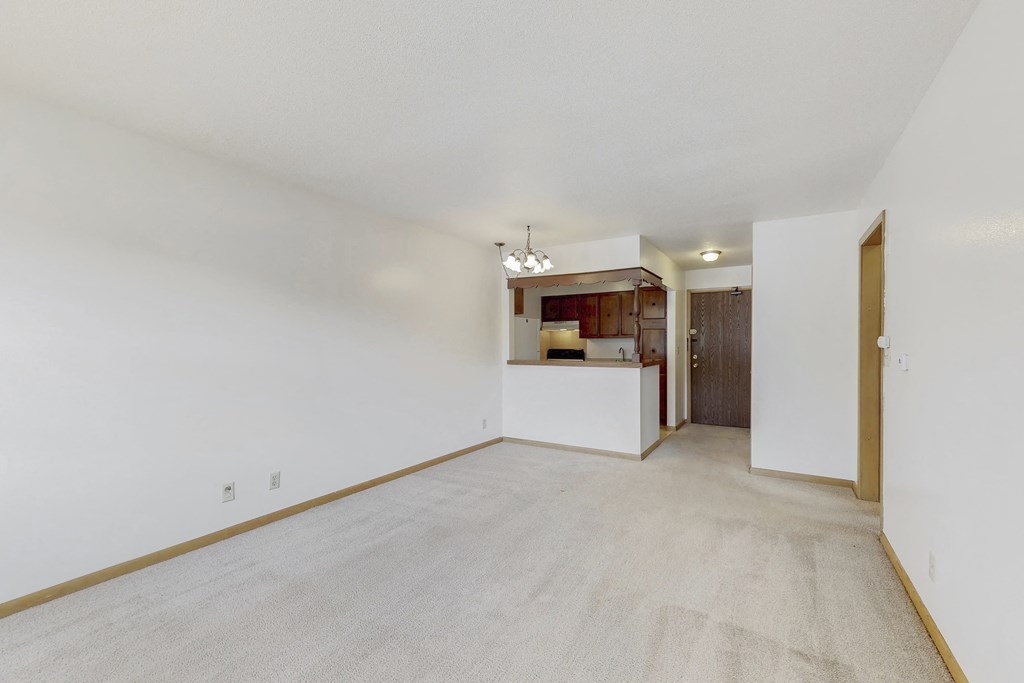 an empty living room with white walls and a kitchen