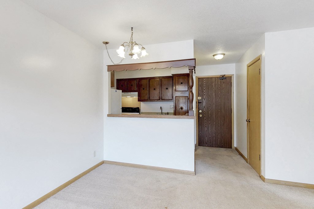 an empty living room with a white wall and a door to a kitchen