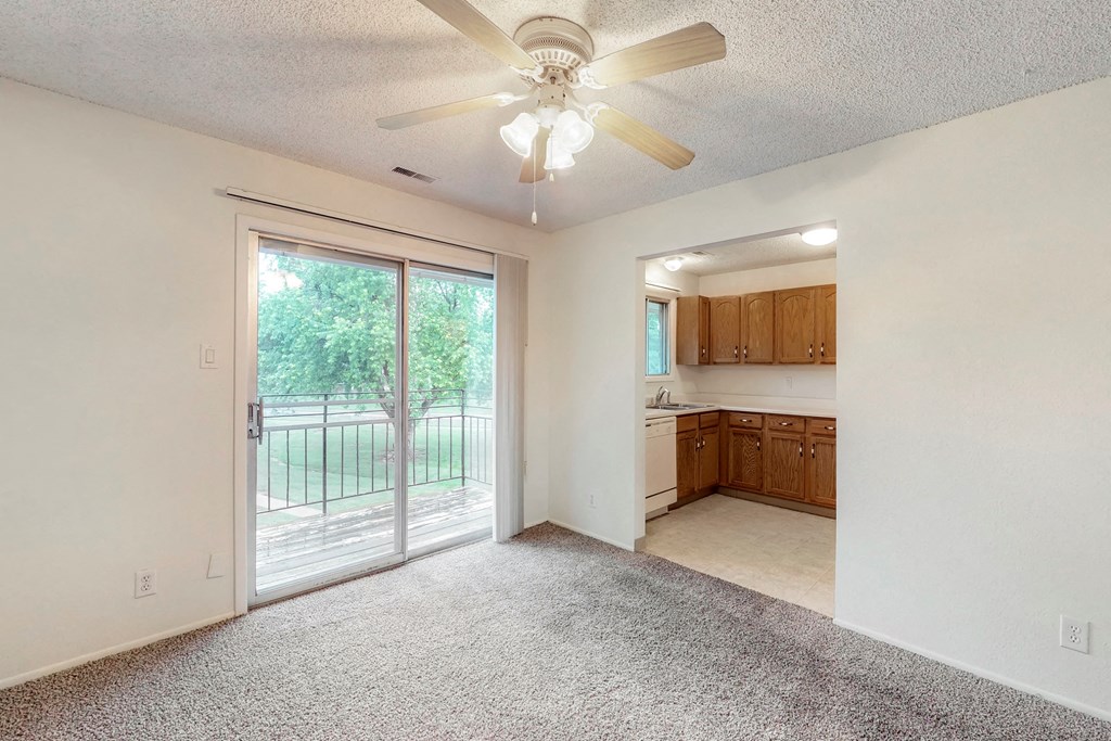 an empty living room with a ceiling fan and a kitchen