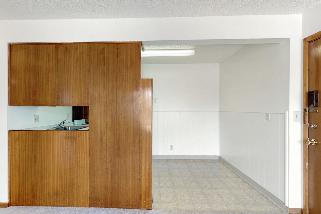 an empty living room with a door to a kitchen