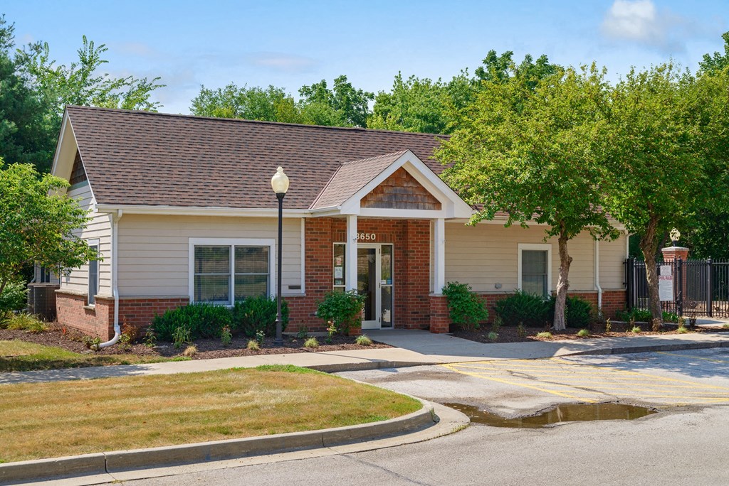 a small tan house with a driveway and trees