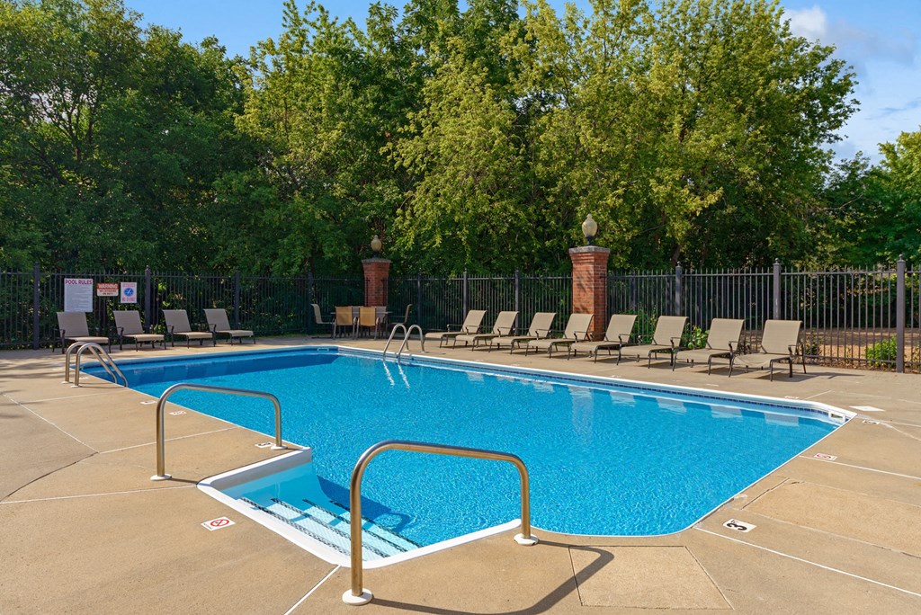 a swimming pool with chaise lounge chairs and a fence with trees