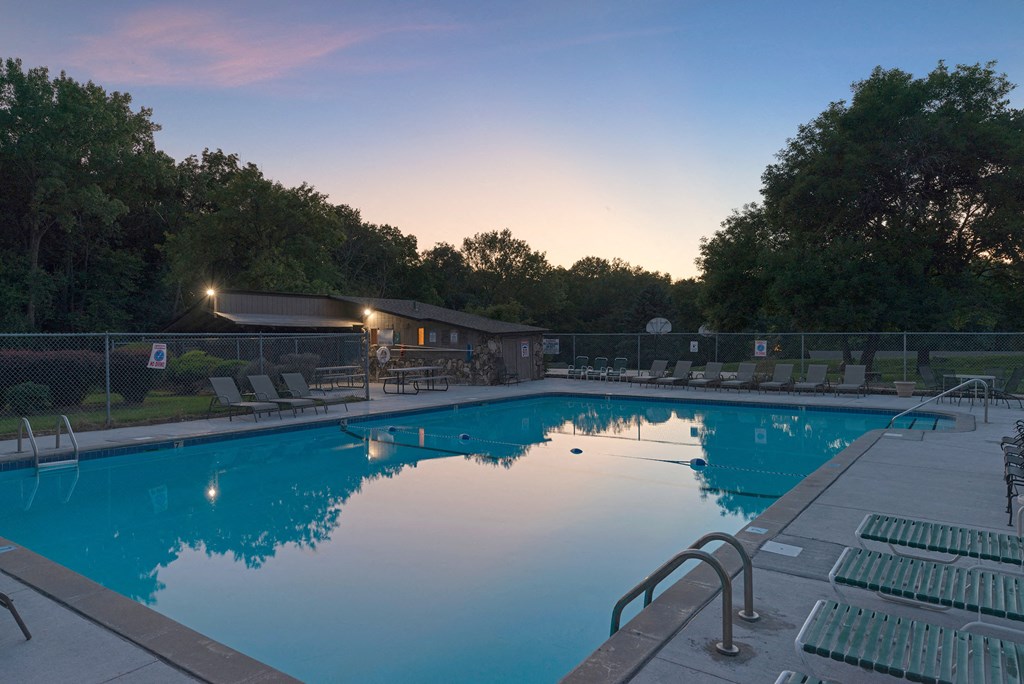 a swimming pool at dusk with chairs around it
