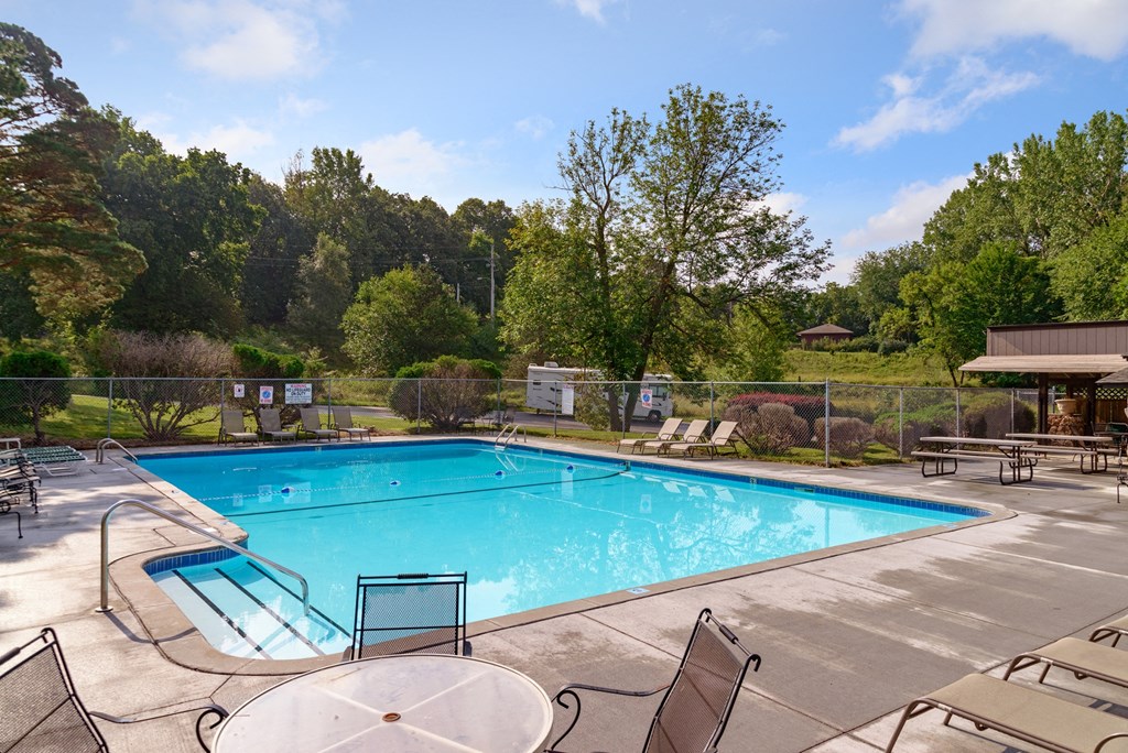 a swimming pool with chairs around it and trees in the background