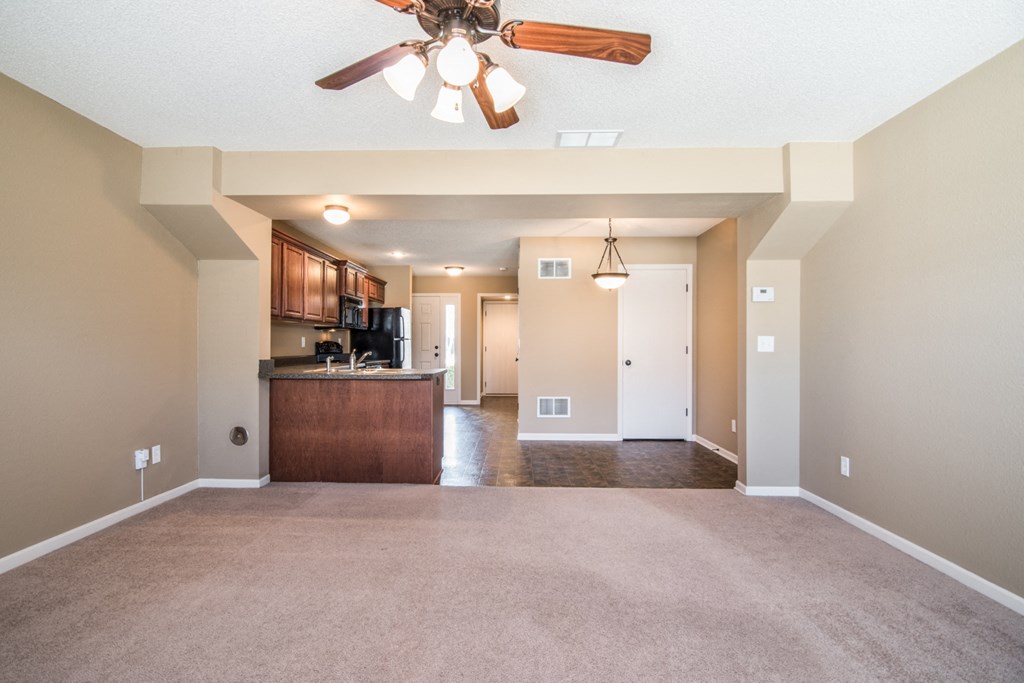 an empty living room with a ceiling fan and a kitchen