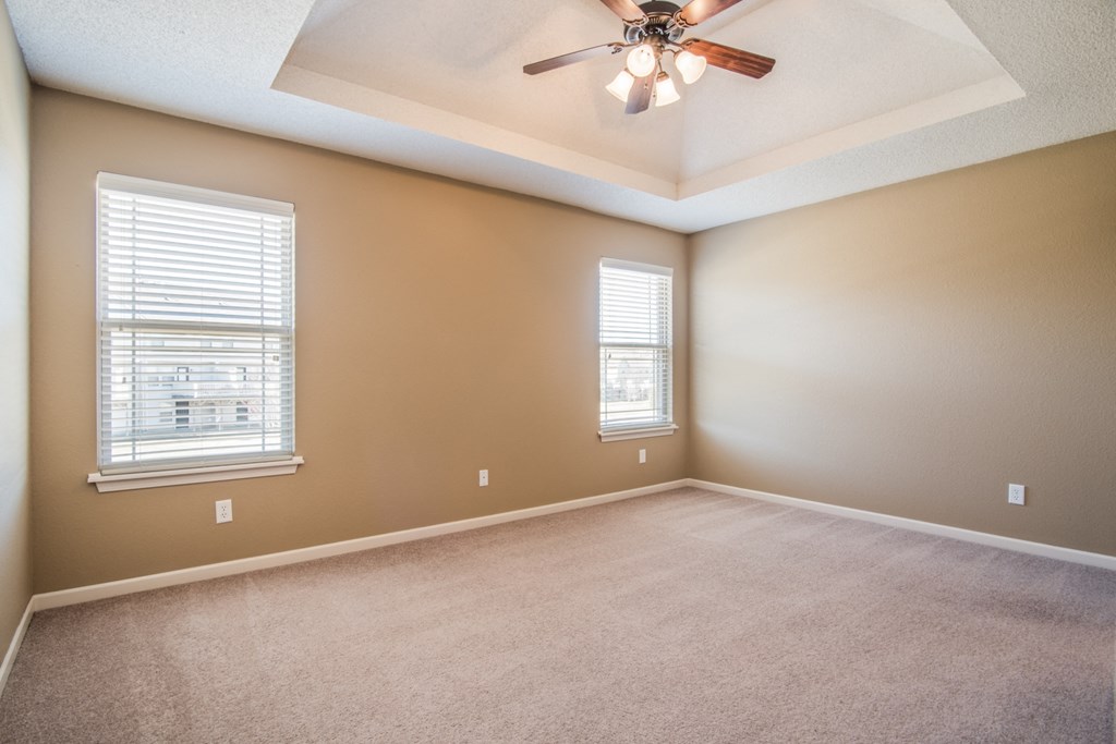 an empty living room with a ceiling fan and two windows