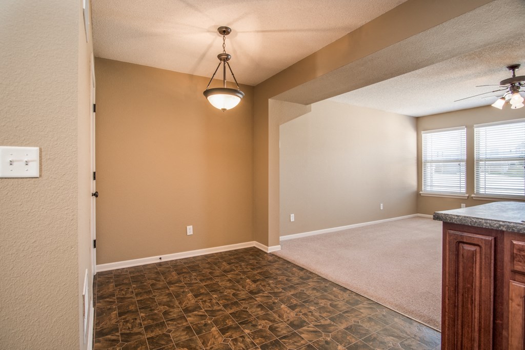 an empty living room with a kitchen and a ceiling fan