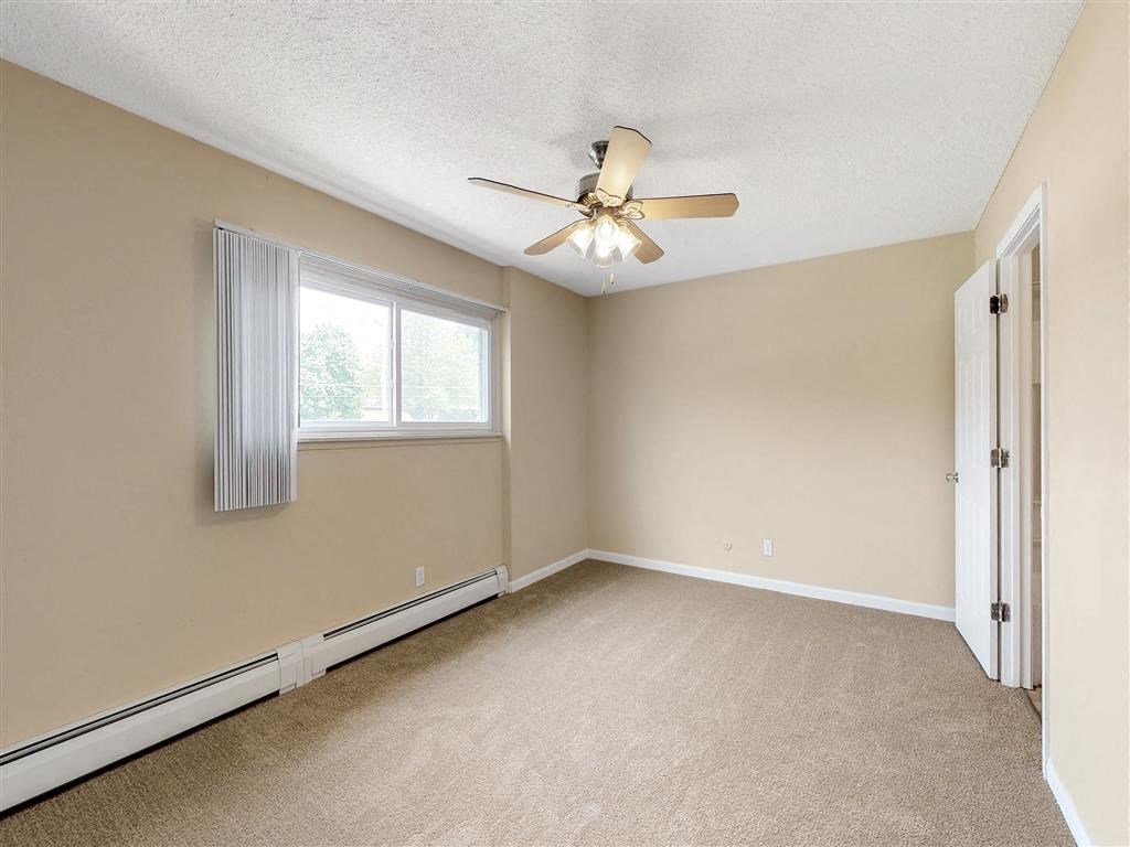 an empty bedroom with a ceiling fan and a window
