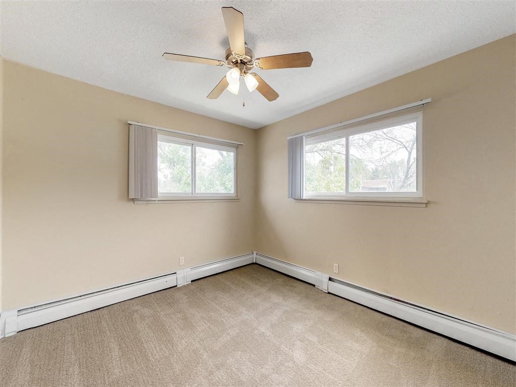 an empty bedroom with a ceiling fan and two windows