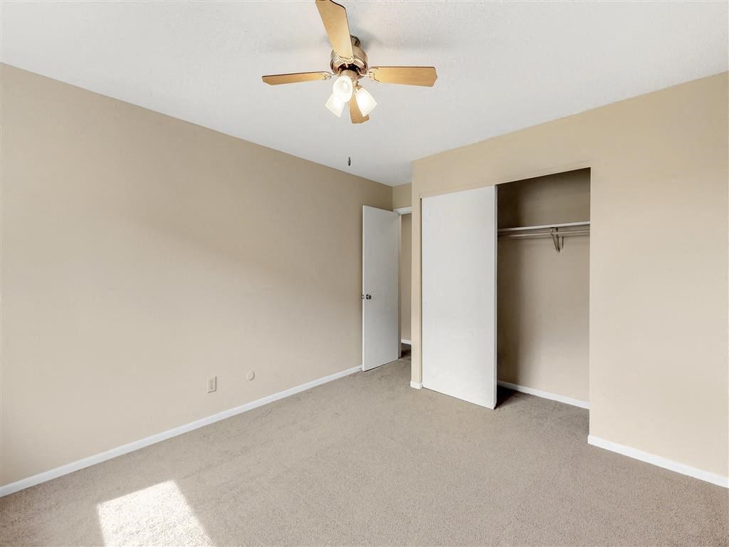 an empty living room with a ceiling fan and a closet