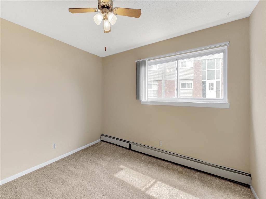 an empty bedroom with a ceiling fan and a window
