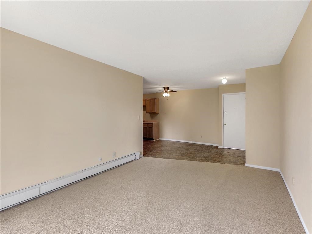 an empty living room with a kitchen in the background