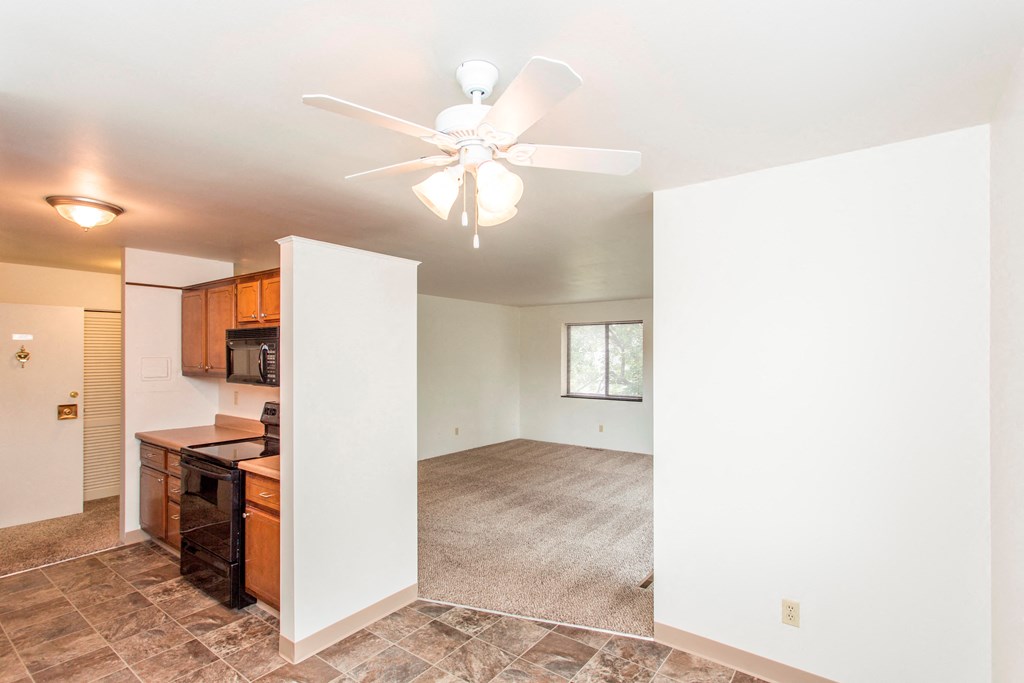 an empty living room with a ceiling fan and a kitchen