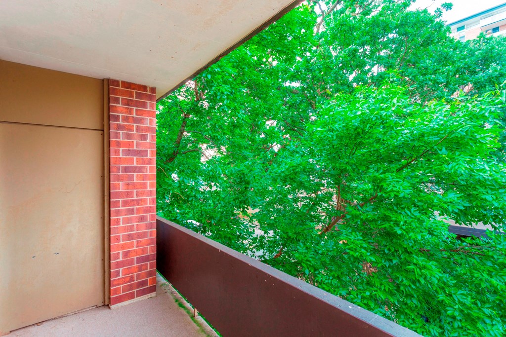 a balcony with a brick wall and a green tree