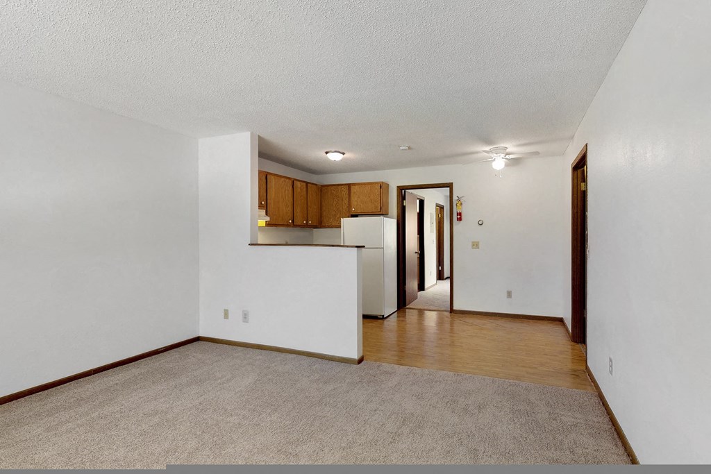 the living room and kitchen of an empty house with white walls and wood flooring