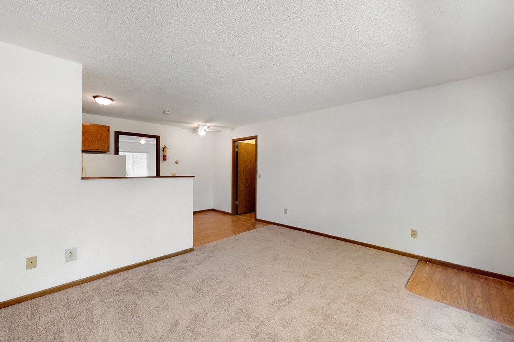 the living room and kitchen of an empty home with white walls and wood flooring