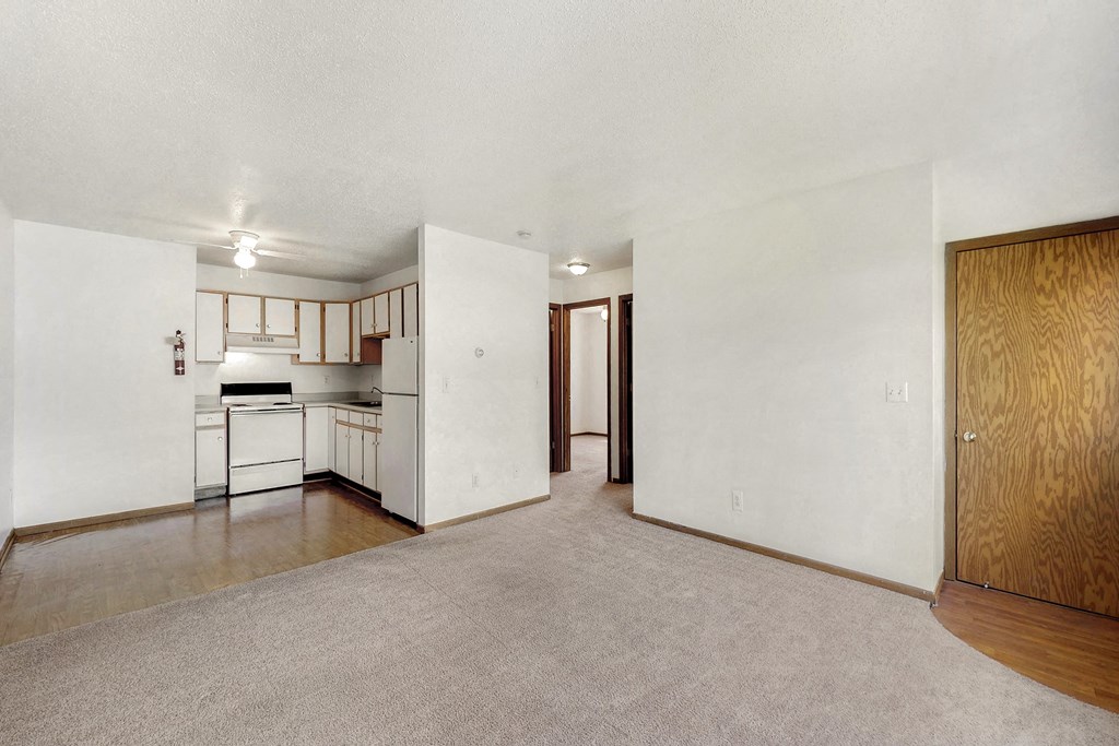 the living room and kitchen of an empty apartment with white walls and wood cabinets