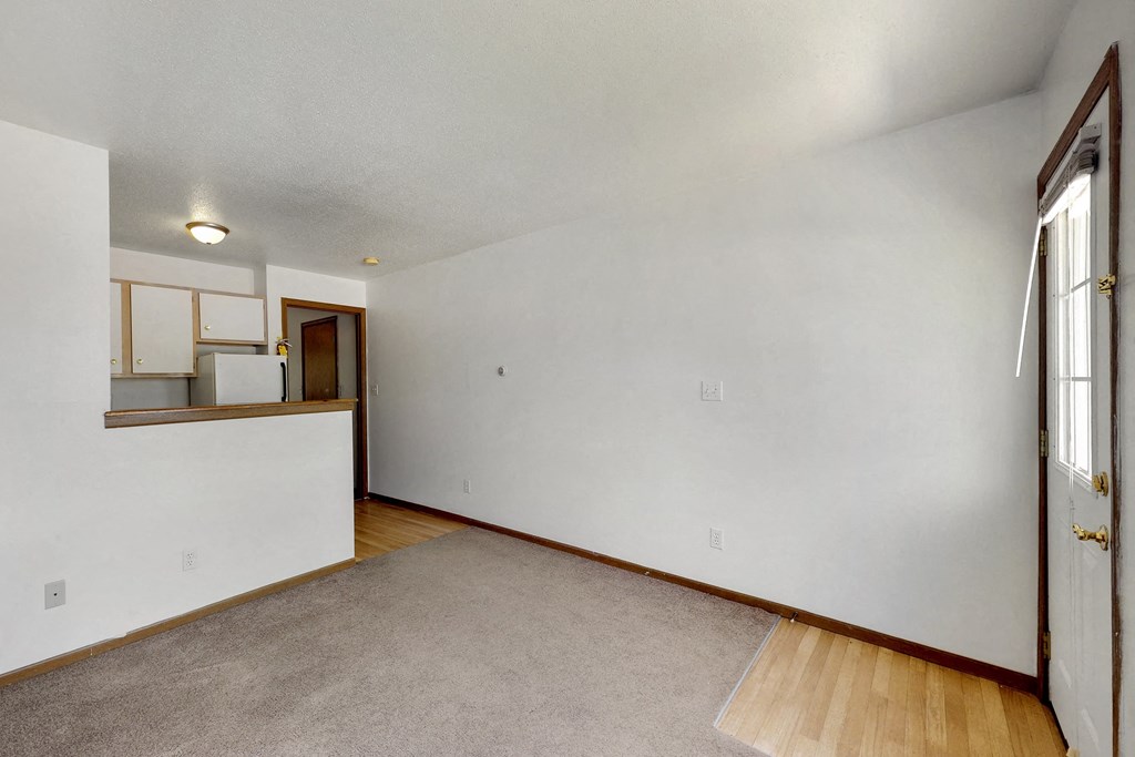 the living room and kitchen of an empty home with white walls and wood floors