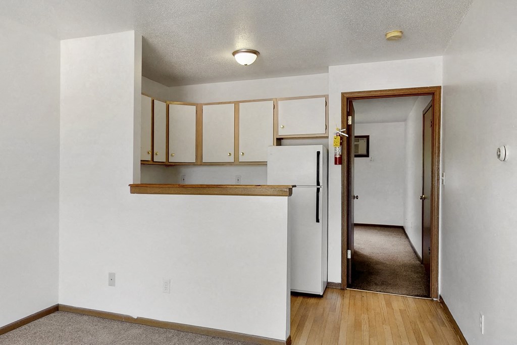 a kitchen with white cabinets and a door to a hallway with a refrigerator