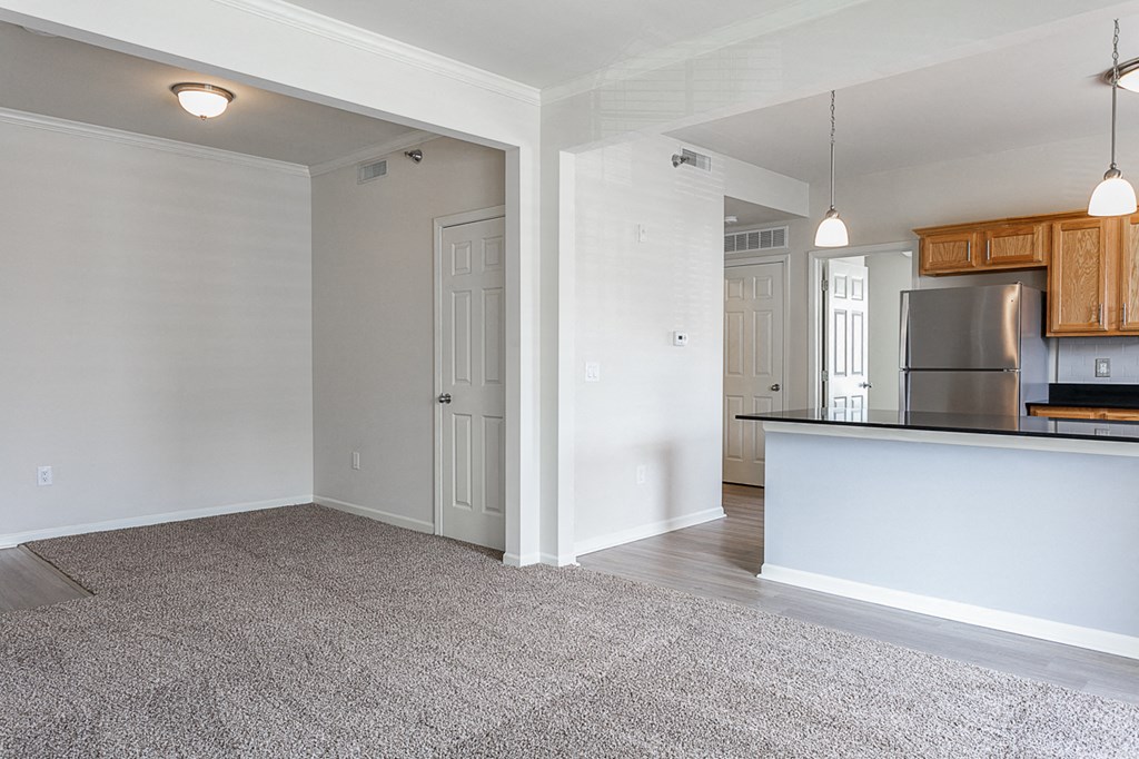 an empty living room with a kitchen in the background
