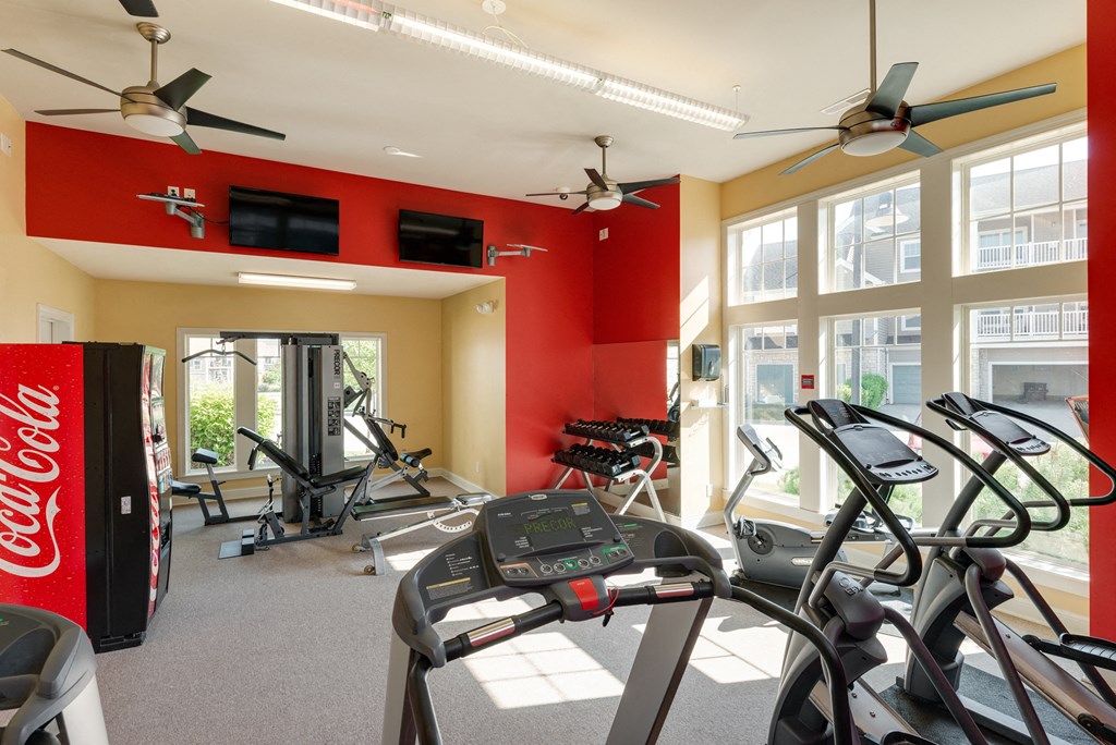 a gym with cardio machines and windows and a coke machine