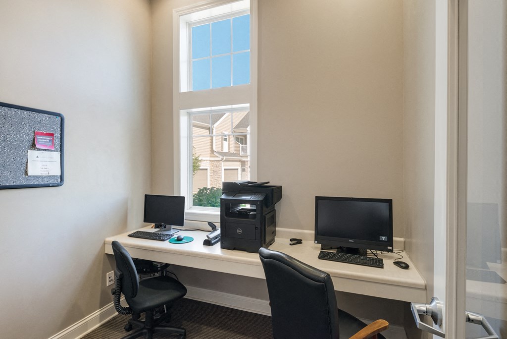 an office with a desk with two computers and a window
