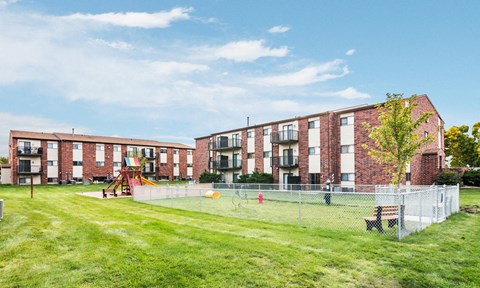 A large grassy area in front of a brick building with a playground.
