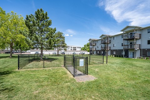 A playground with a swing set in the middle of a grassy area with trees and apartment buildings in the background.