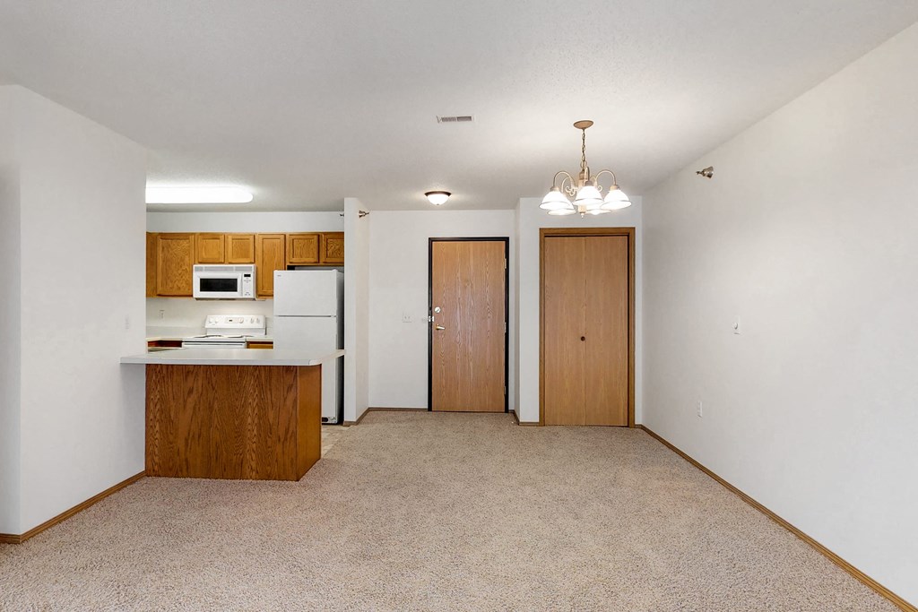 an empty living room with a kitchen and a door to a closet
