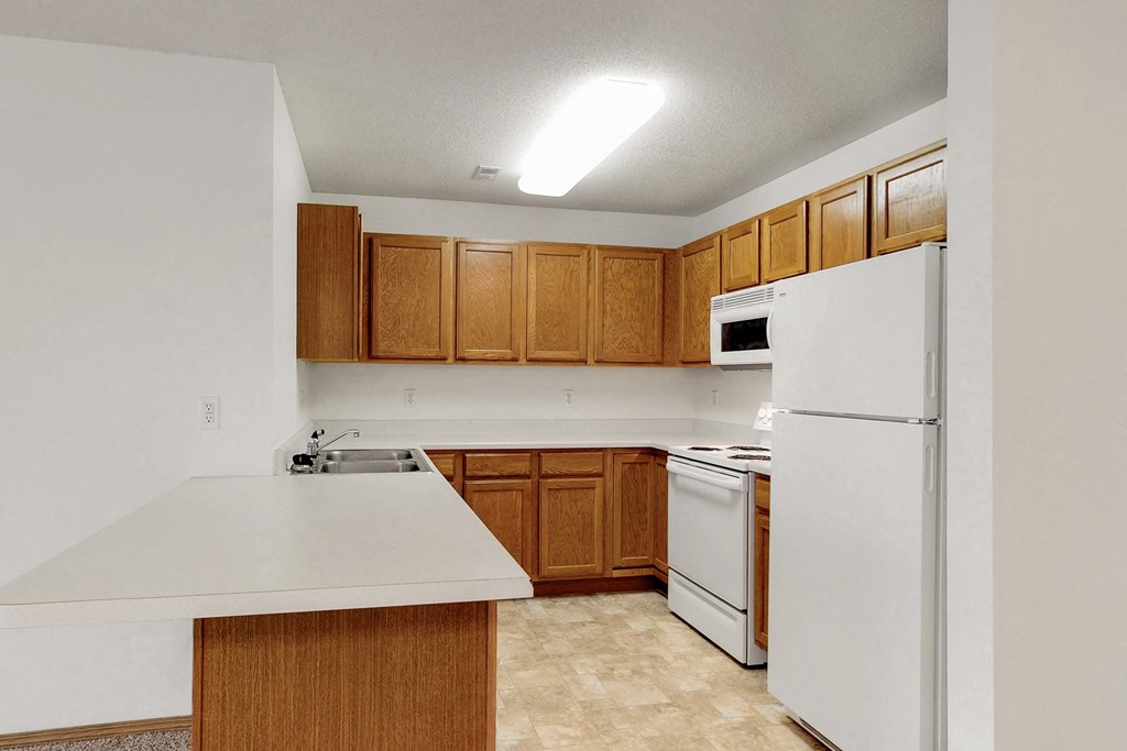 an empty kitchen with white appliances and wooden cabinets